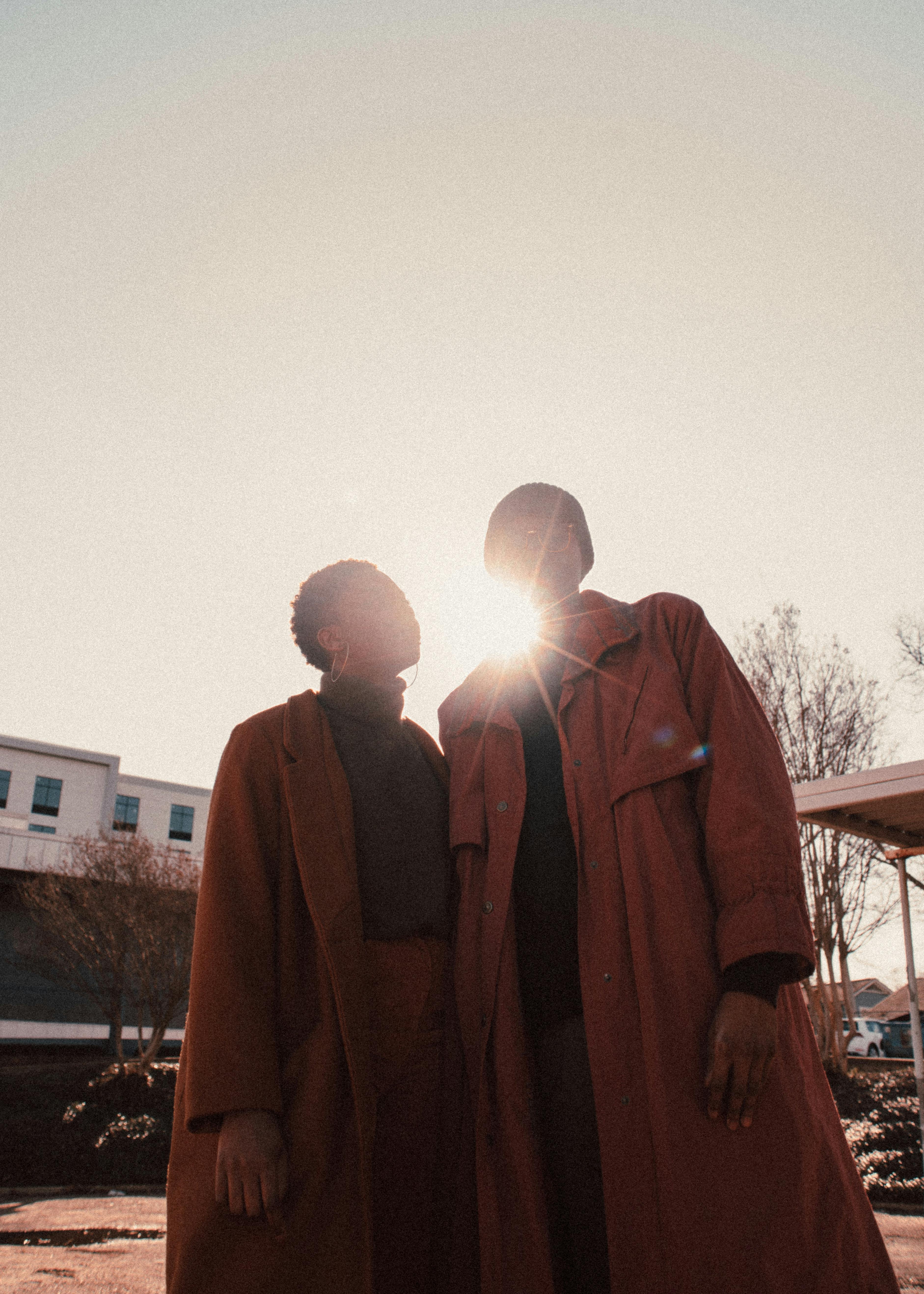 Silhouette of two people in coats standing against bright sunlight, capturing an autumn vibe.