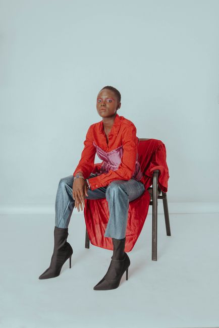 Stylish African woman poses confidently in red top and jeans, seated in a studio.