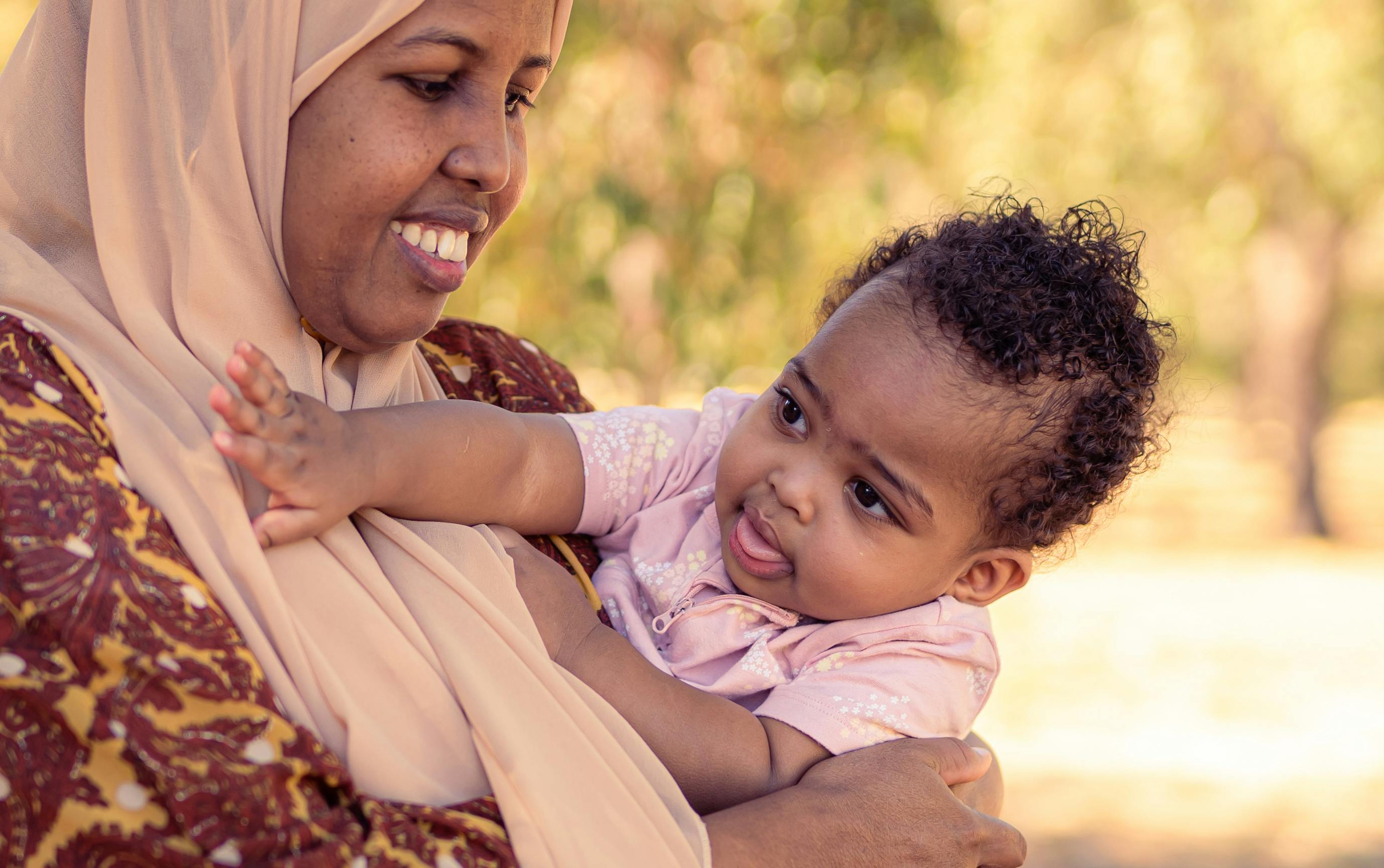A joyful mother holding her baby in a park setting, capturing a tender moment of bonding.