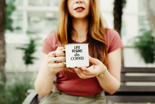 Free Close-up of a woman holding a coffee mug with text outdoors, creating a casual and inviting vibe. Stock Photo