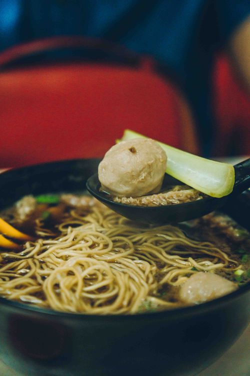 Free Close-up of a bowl of Asian noodle soup with vegetables in a vibrant, cozy setting. Stock Photo