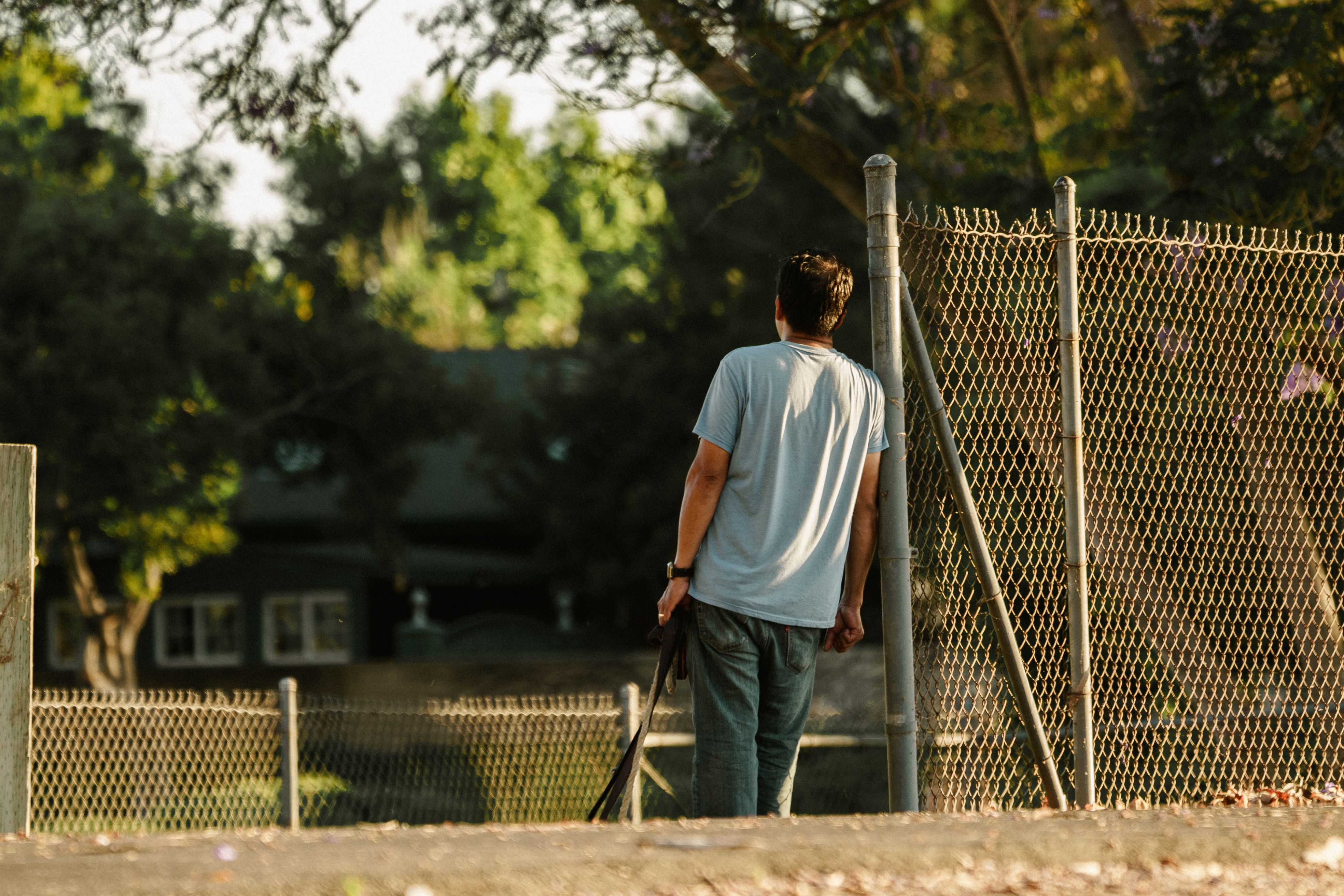 Back View of a Man Leaning against a Fence Pole · Free Stock Photo