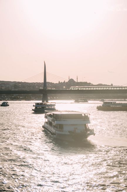 Boats cruising on the shimmering Golden Horn with a scenic bridge at sunset.