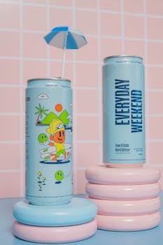 Two lime and soda beverage cans with a fun design on a pastel pink tiled background.