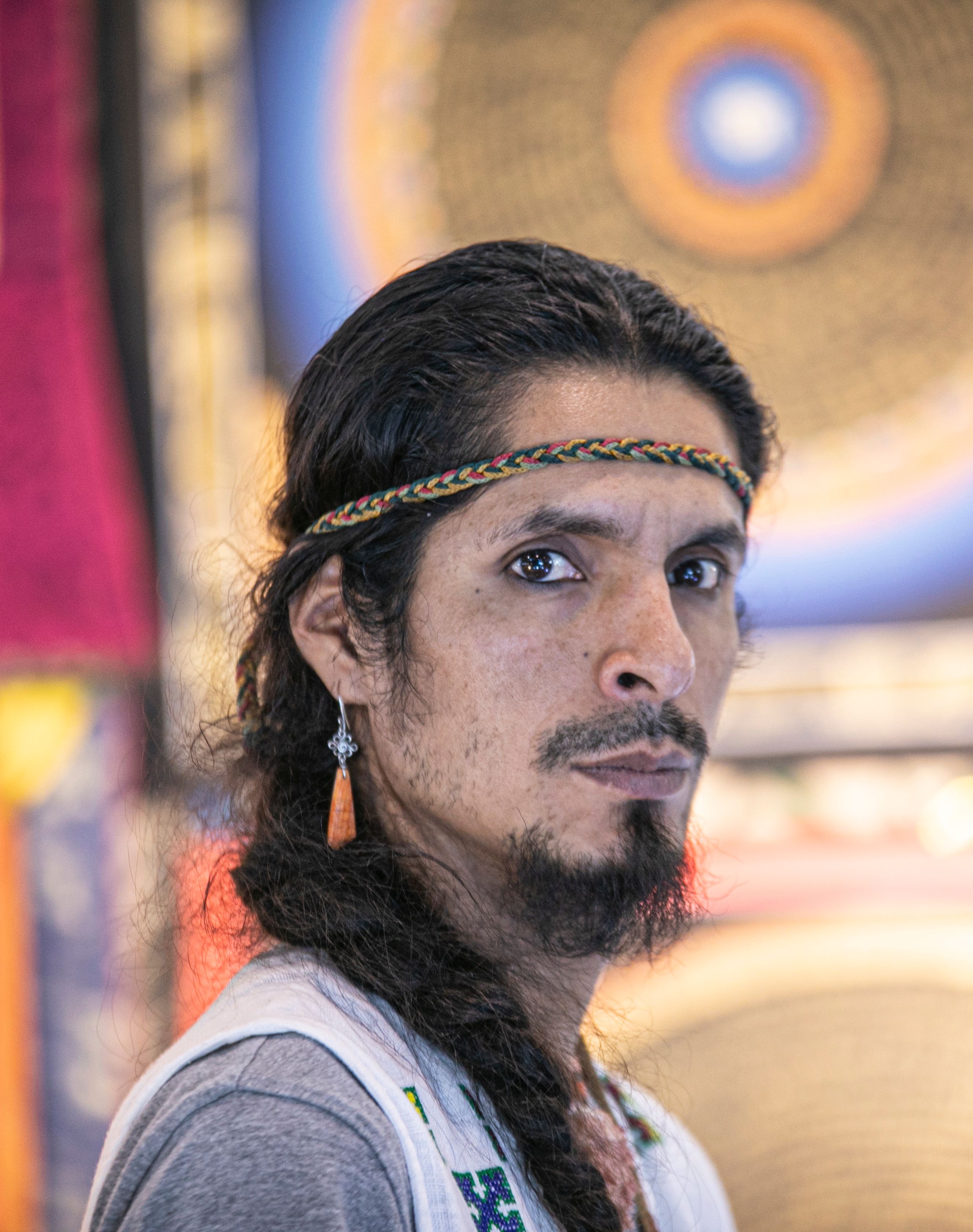 Profile portrait of a man with braided hair and a decorative headband in a colorful setting.