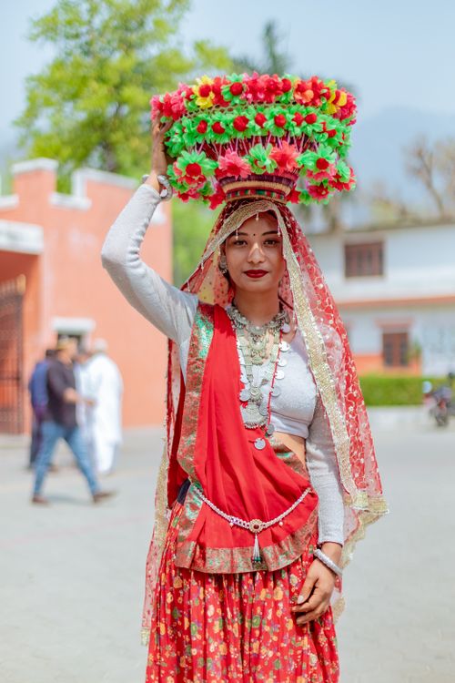 Free A woman in vibrant traditional attire stands outdoors with a colorful floral basket on her head. Stock Photo