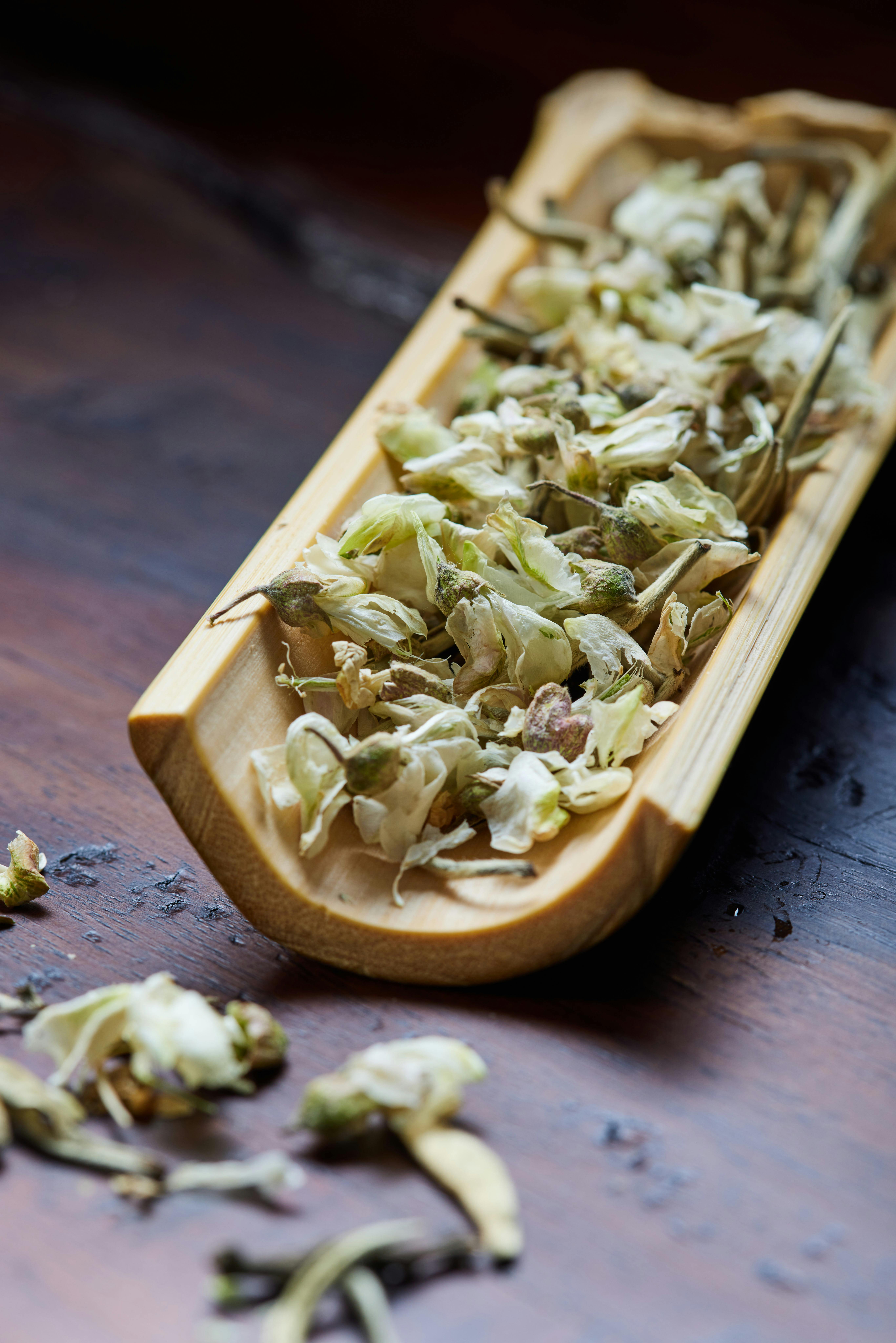 Close-up of dried herbal leaves in a wooden tray on a rustic surface.