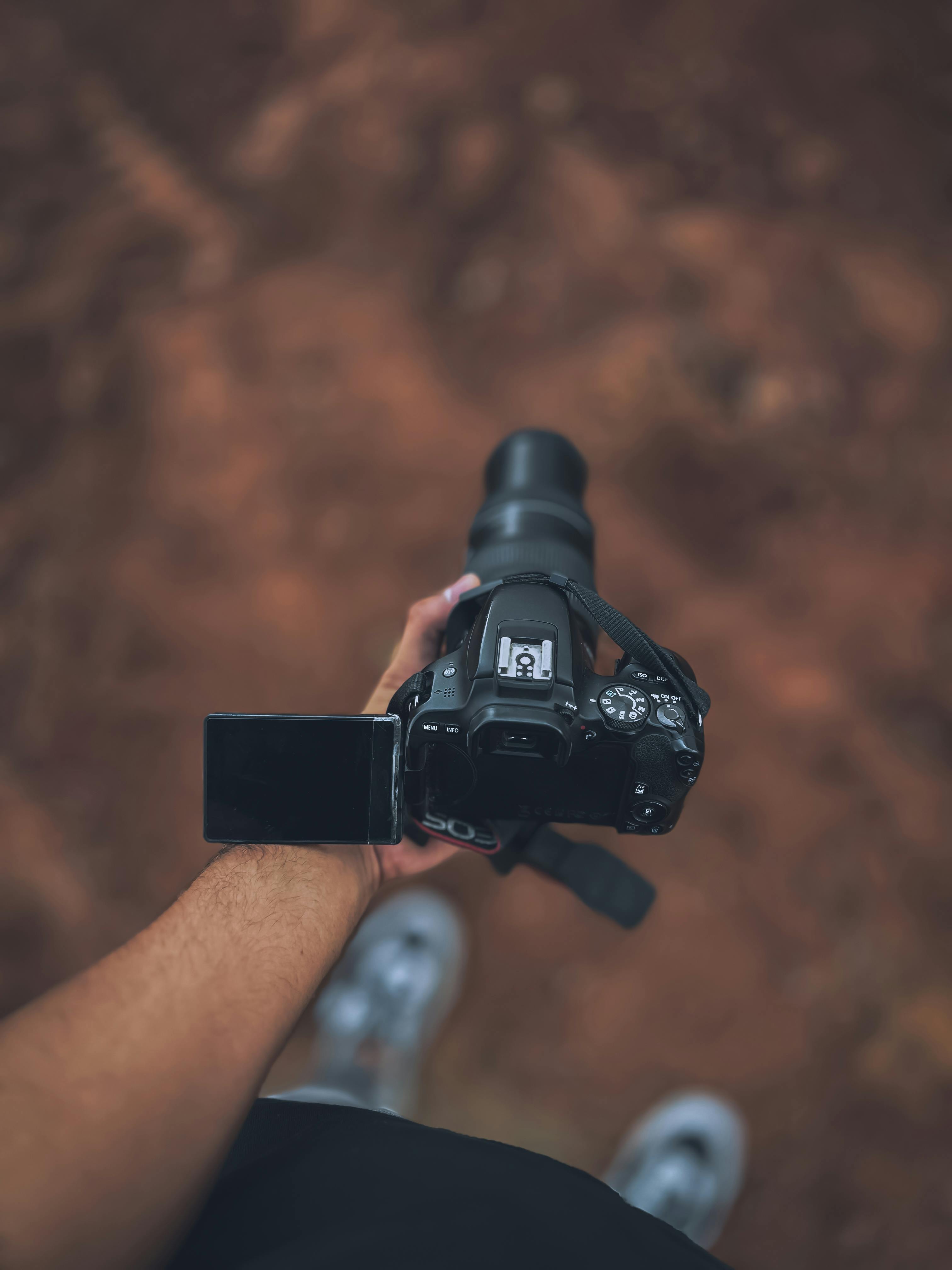 Top view of a person holding a DSLR camera with an adjustable screen outdoors, ready to shoot.