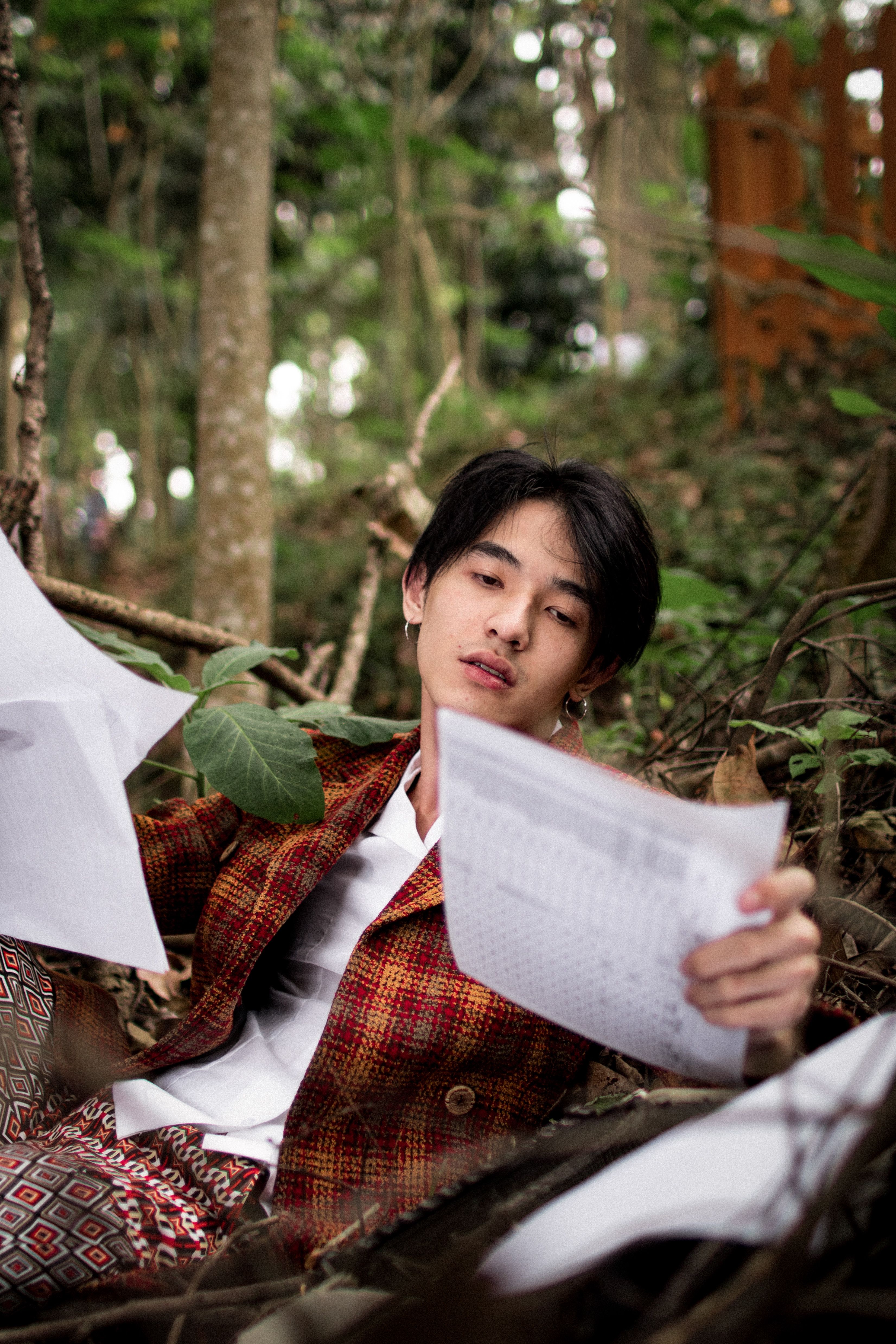 Casual young man reading documents amidst a natural forest environment.