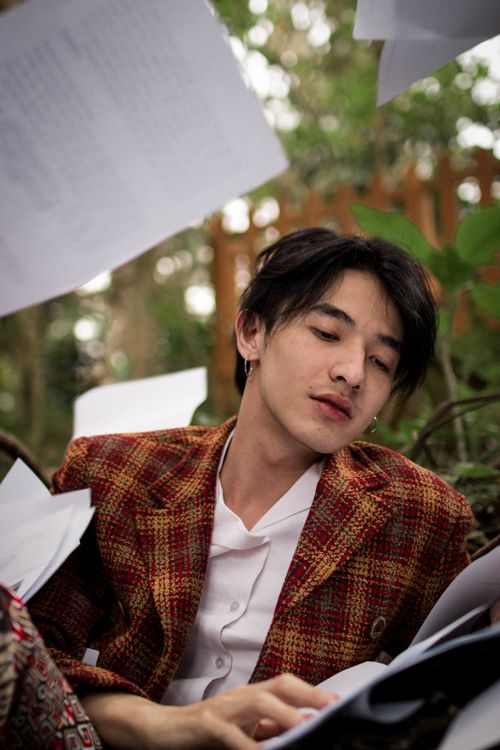 Free Casual young man in a plaid jacket relaxing amidst flying papers in an outdoor setting. Stock Photo