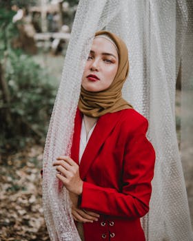 Stylish woman posing outdoors in a red blazer and hijab, exuding elegance and confidence.