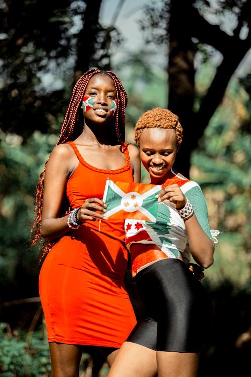 Free Two women celebrate with the Burundi flag and face painting in a vibrant outdoor setting. Stock Photo