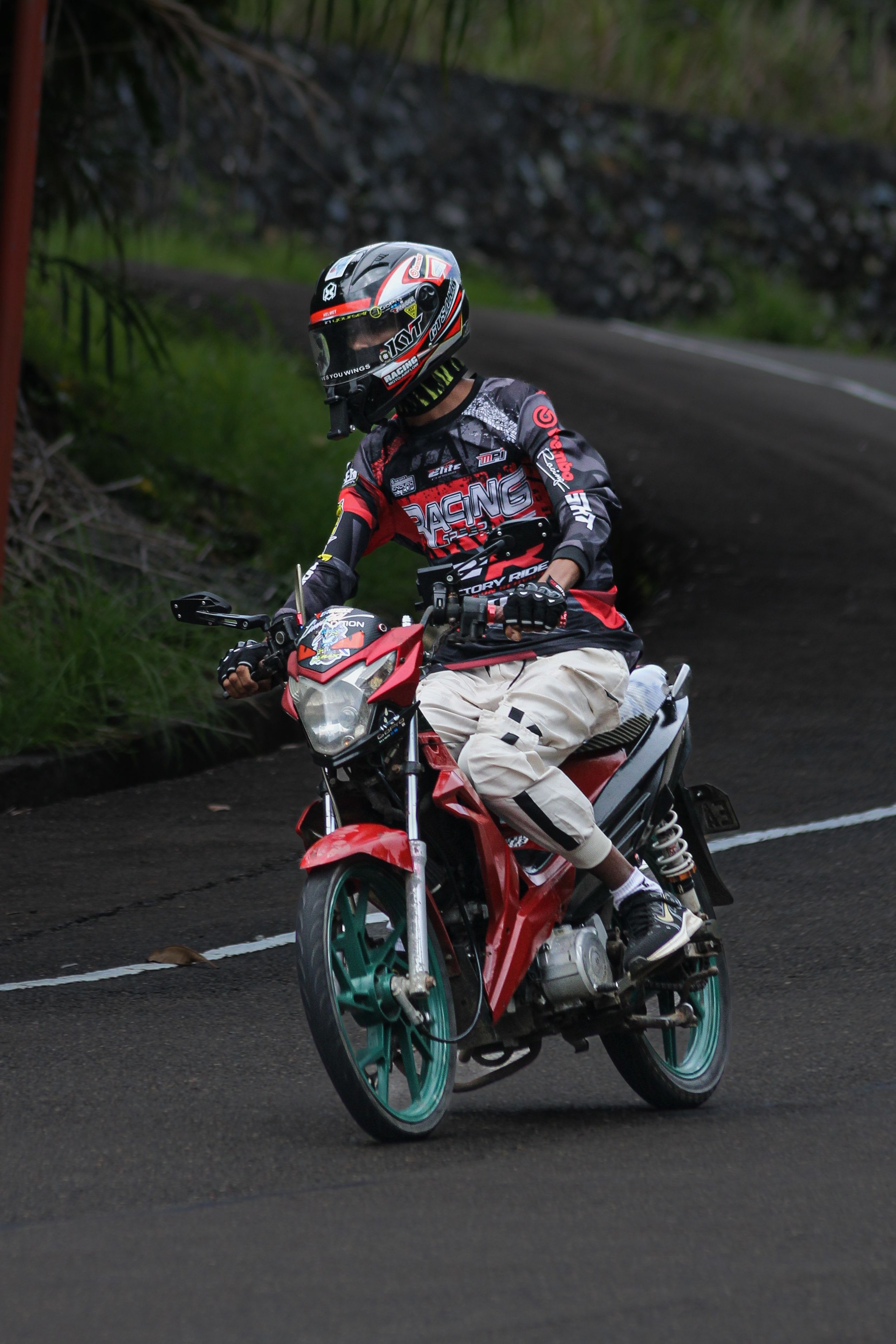 Motorcyclist wearing gear on a winding outdoor road with scenic background.