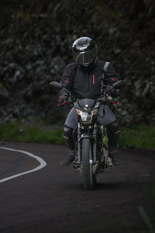 Free A biker clad in black gear rides a motorcycle on a winding forest road. Stock Photo