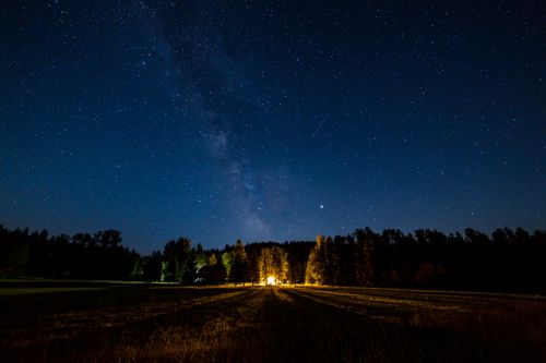 Free Peaceful starry night sky over a forest with a glowing campfire, highlighting the Milky Way. Stock Photo