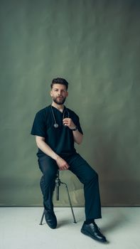 Portrait of a young male doctor sitting indoors with a stethoscope, wearing a healthcare uniform.