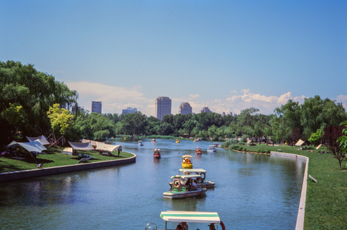 Free Colorful pedal boats on a sunny day in Chaoyang Park, Beijing, with city skyline. Stock Photo