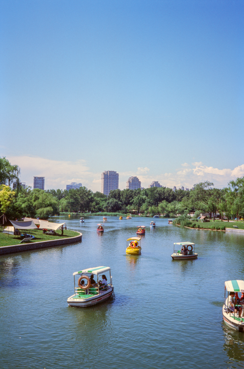 Free Enjoy a sunny day boating on the river in Chaoyang Park, Beijing, with a cityscape backdrop. Stock Photo