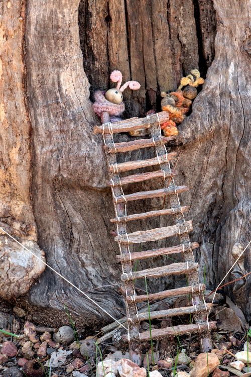 Free Whimsical toys nestled in a tree hollow with a rustic ladder, showcasing a playful countryside scene. Stock Photo