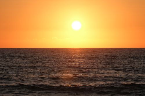 Free A beautiful sunset over the ocean with a warm golden glow, creating a peaceful seascape. Stock Photo