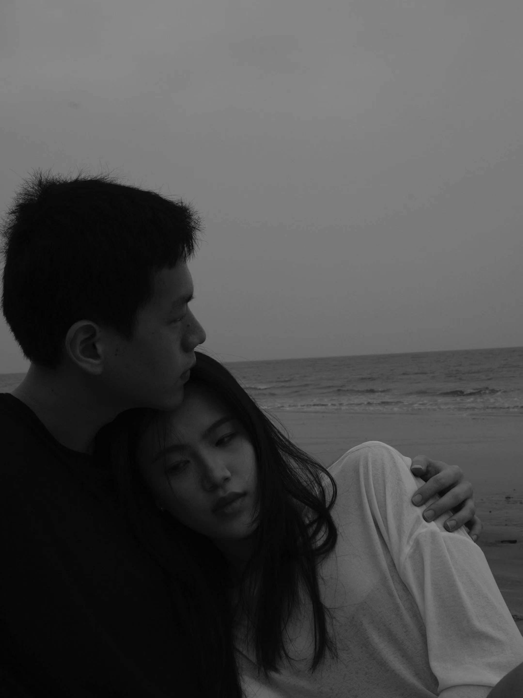 Young couple embracing on a serene beach in a moody black and white photograph.