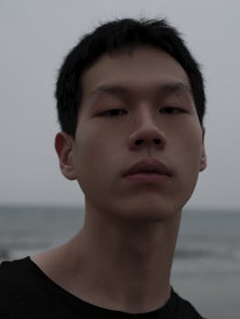 Moody portrait of a young adult by the sea at twilight, exuding calm introspection.