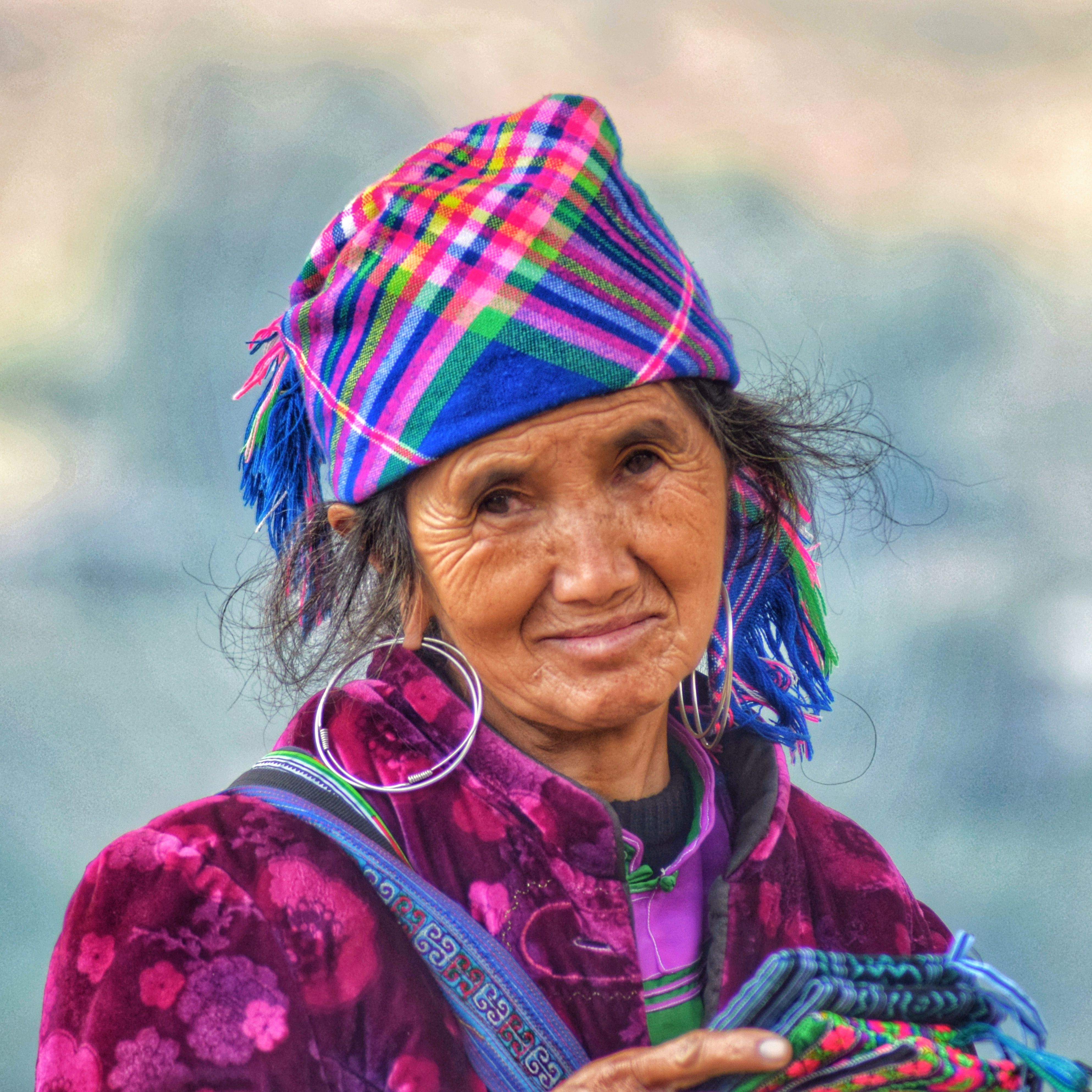 Portrait of an elderly woman wearing traditional colorful clothing and accessories, smiling warmly outdoors.