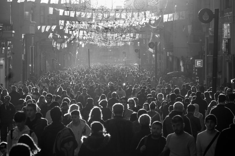Black and white photo of a busy urban street packed with pedestrians in sunlight.
