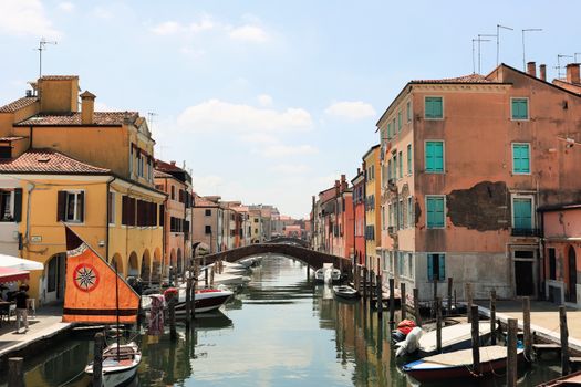 Picturesque canal scene in Chioggia with colorful buildings and boats under a sunny sky.