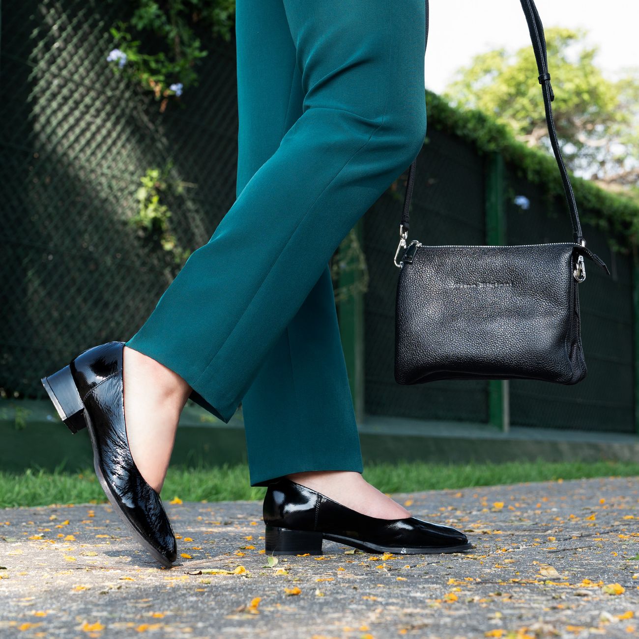Mulher fashionista em calças verdes e sapatos pretos caminhando ao ar livre, exibindo elegância e estilo.