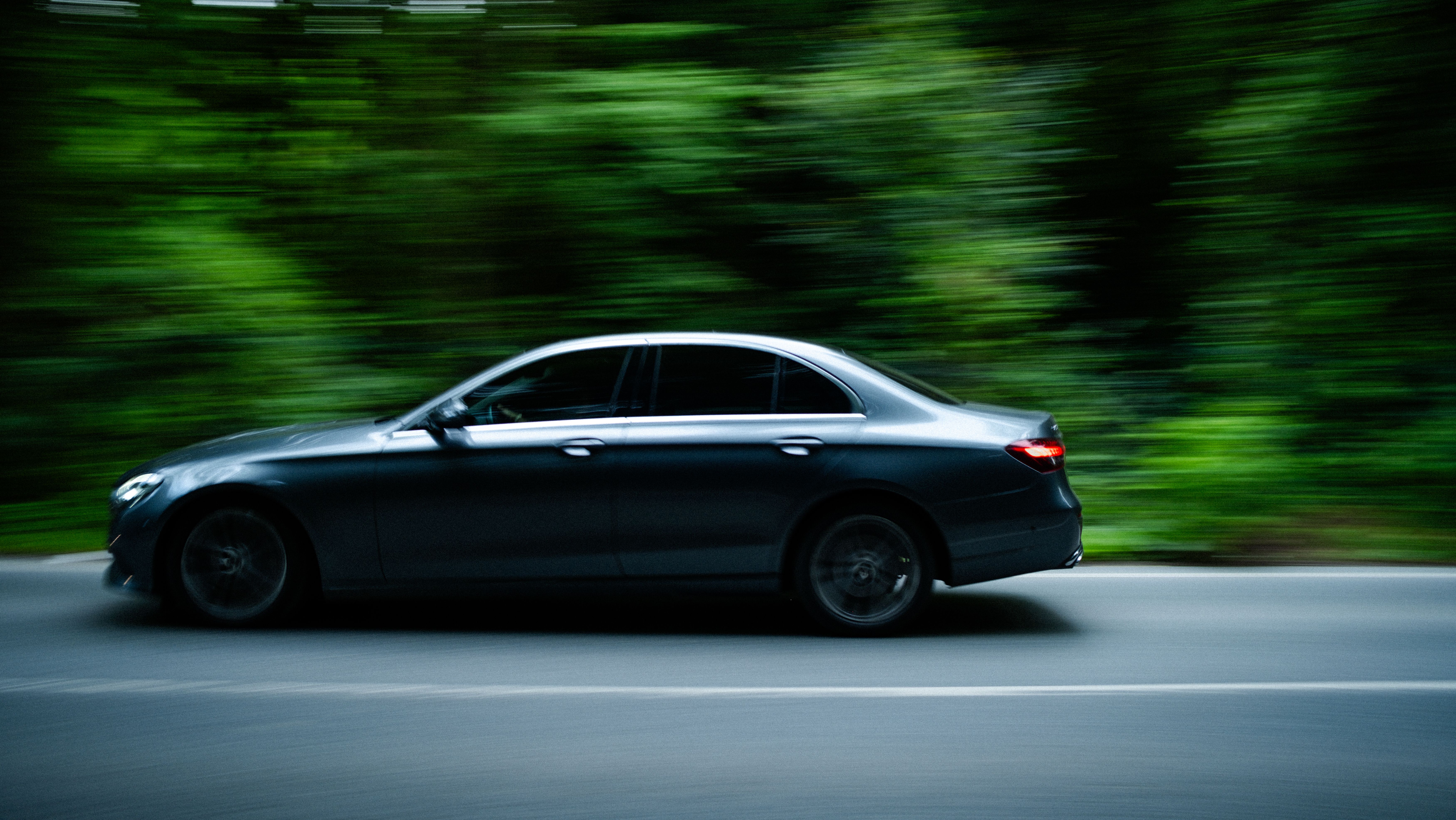 A black car driving on a road in the woods · Free Stock Photo