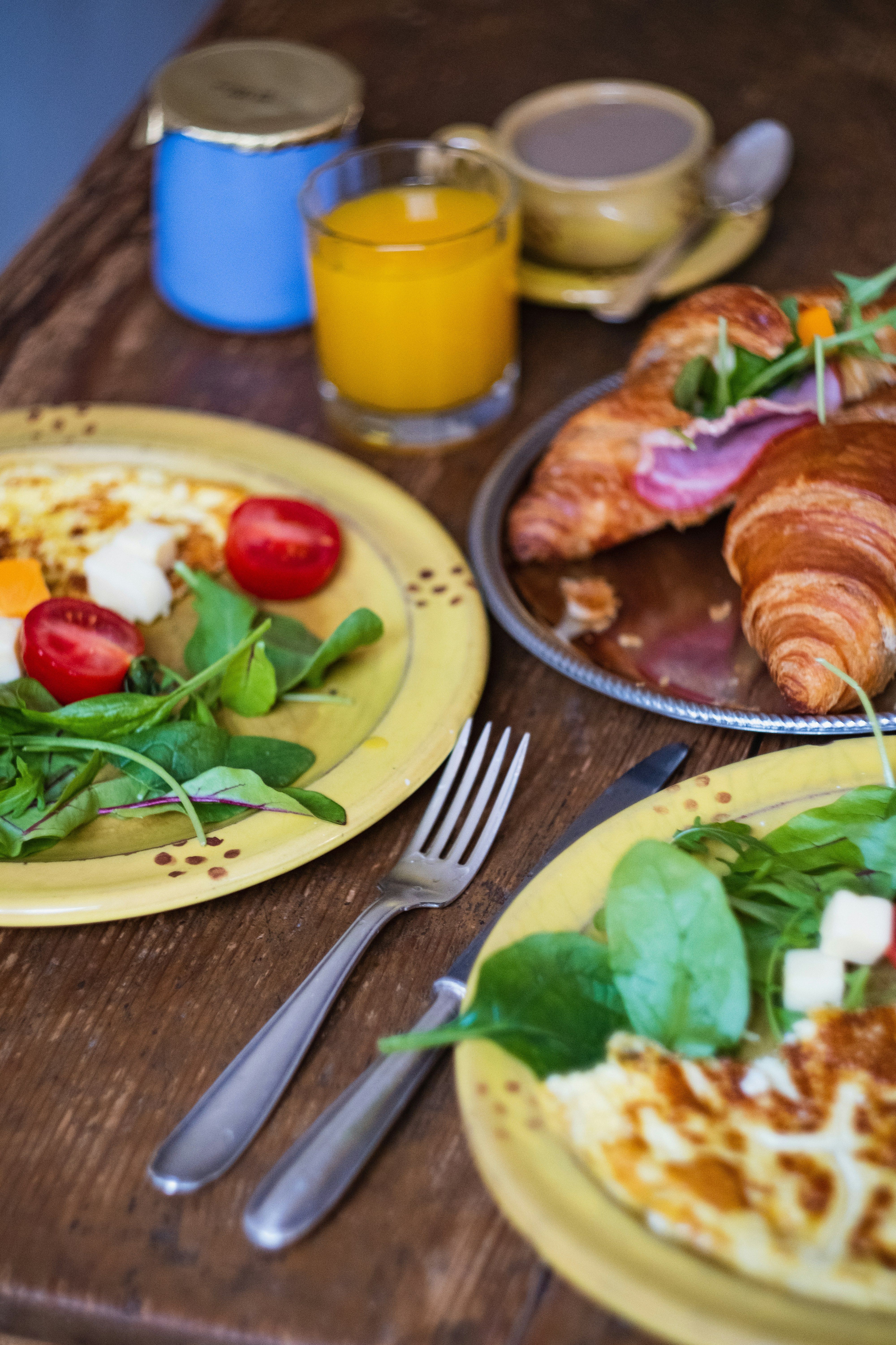 A vibrant French breakfast featuring croissants, salad, cheese, and juice on a rustic table.