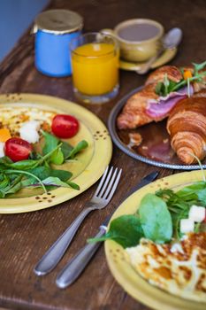 A vibrant French breakfast featuring croissants, salad, cheese, and juice on a rustic table.