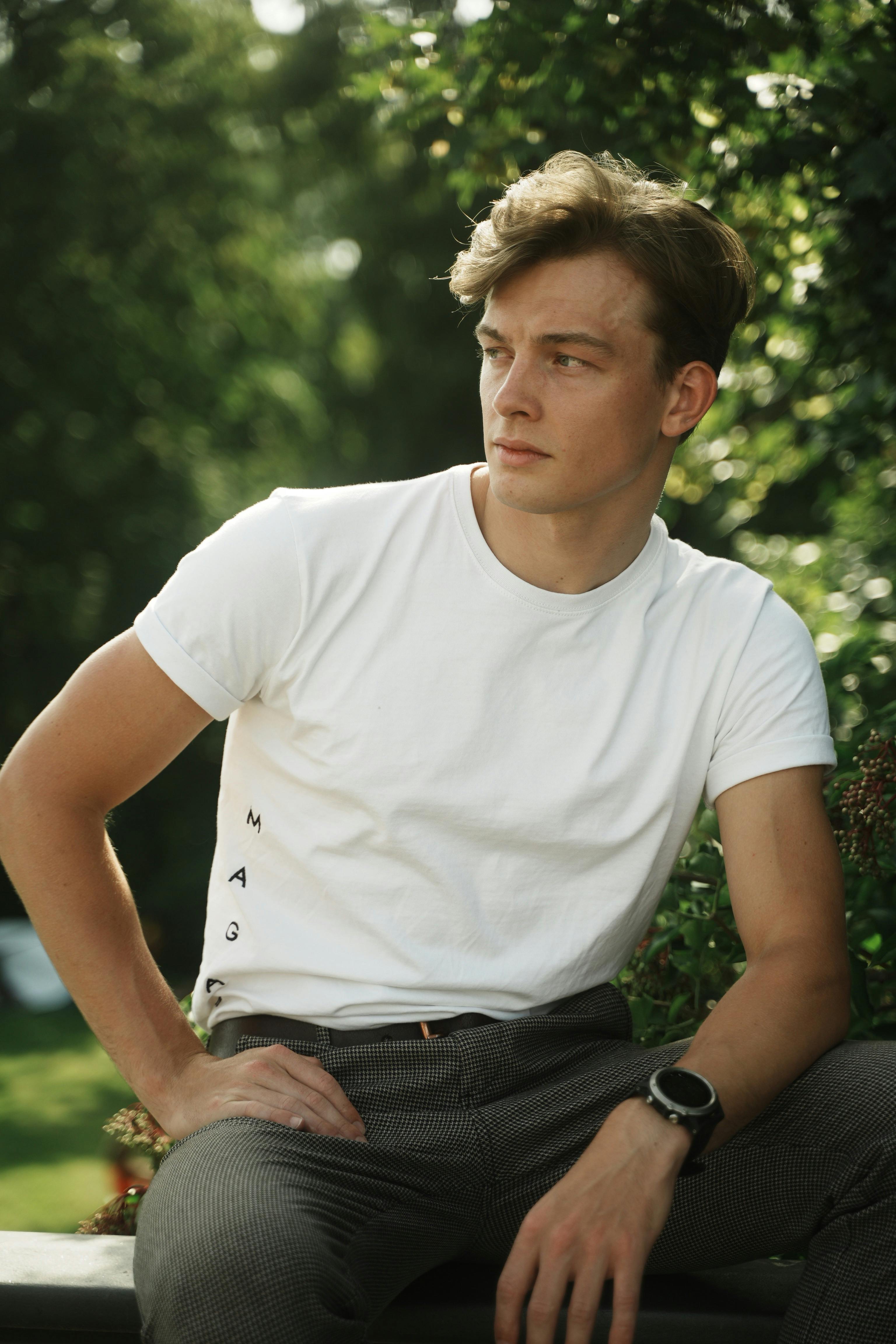 Portrait of a young man sitting outdoors in white t-shirt and plaid pants, enjoying a sunny day.