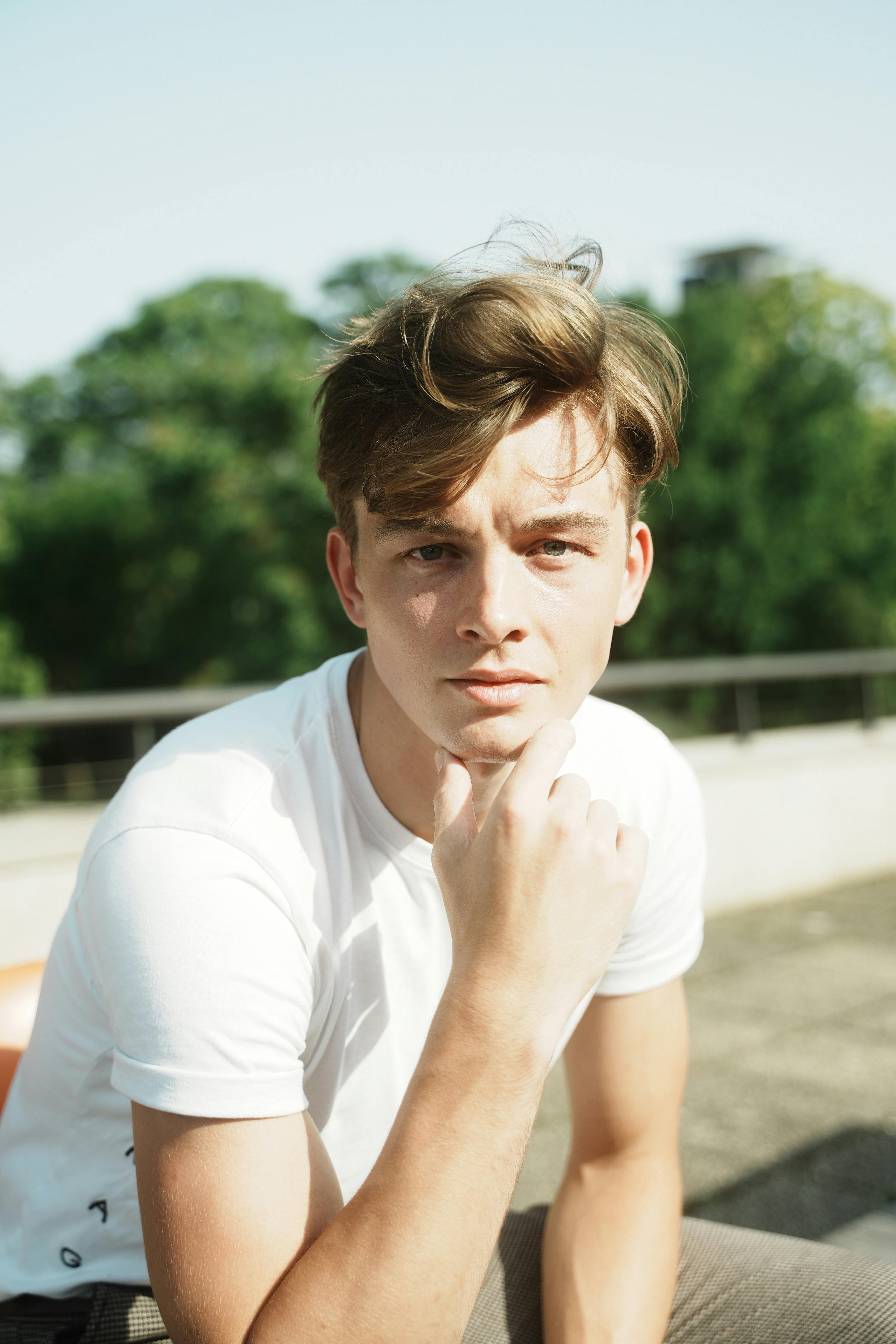 Casual portrait of a young man outdoors in natural sunlight, wearing a white t-shirt.