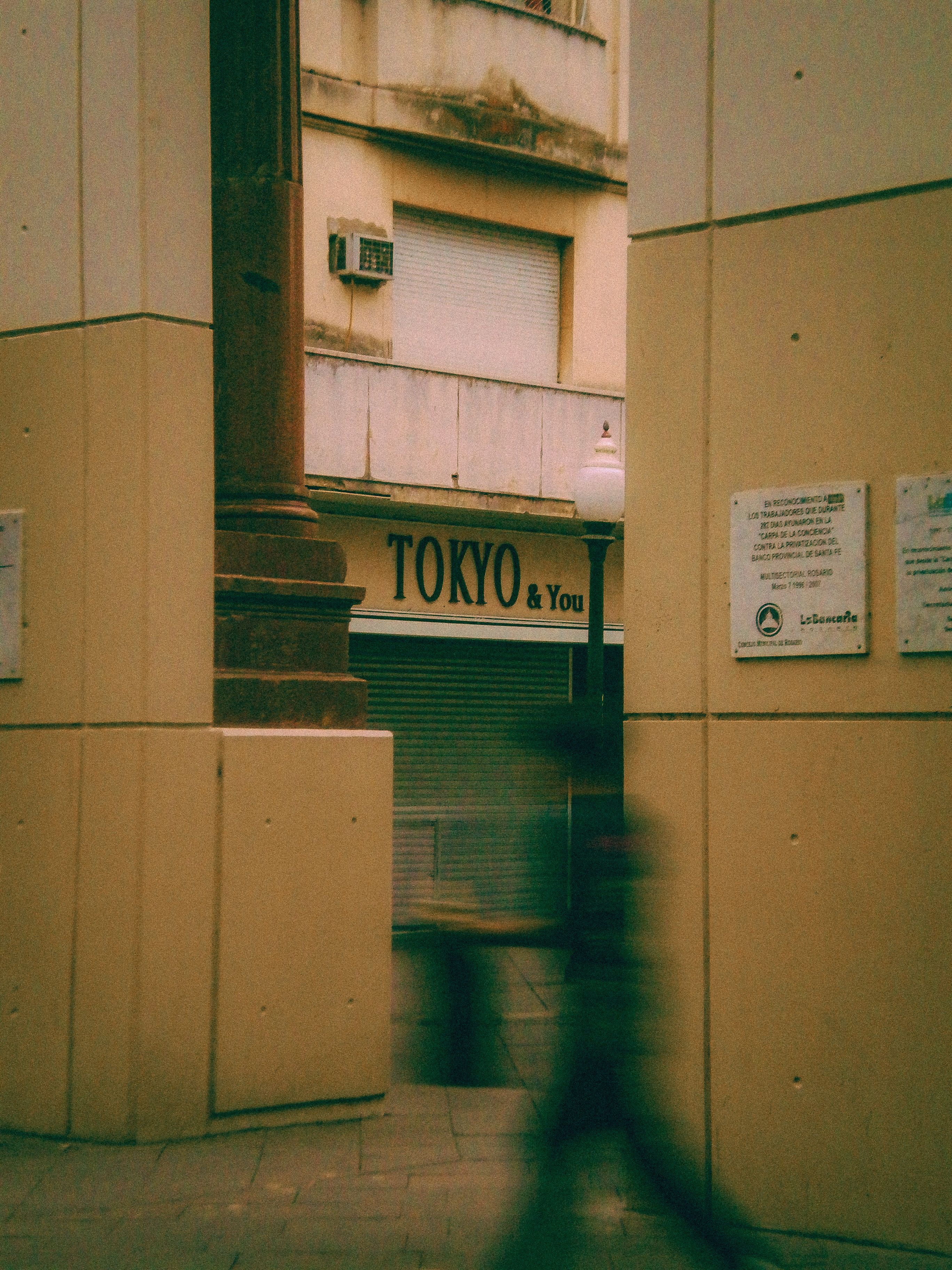 Blurred motion of a person walking in a narrow alley in Rosario, Argentina, featuring urban architecture.