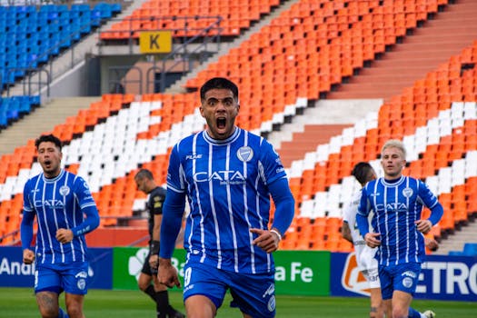 Soccer players in blue jerseys celebrate scoring a goal in an empty stadium.