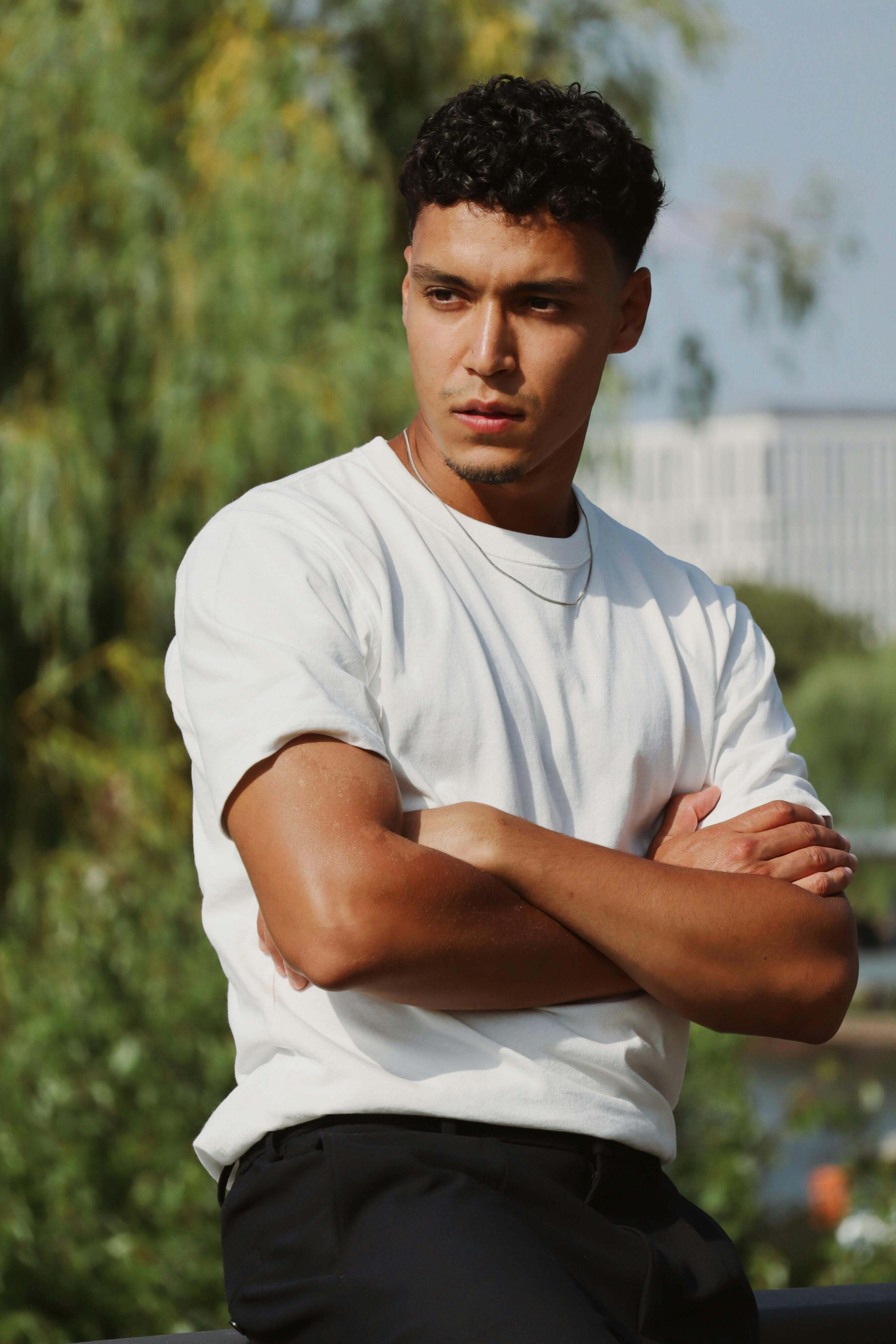 Portrait of a young man posing outdoors in Berlin, exuding confidence with arms crossed.