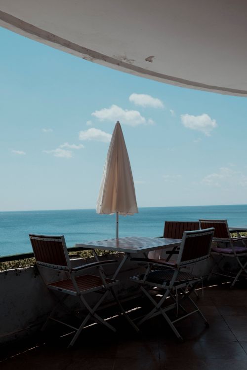 Free Relax on a serene balcony with ocean views, shaded by a sun umbrella. Stock Photo