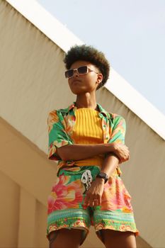 A fashionable young woman poses outdoors in Berlin with colorful summer attire and sunglasses.