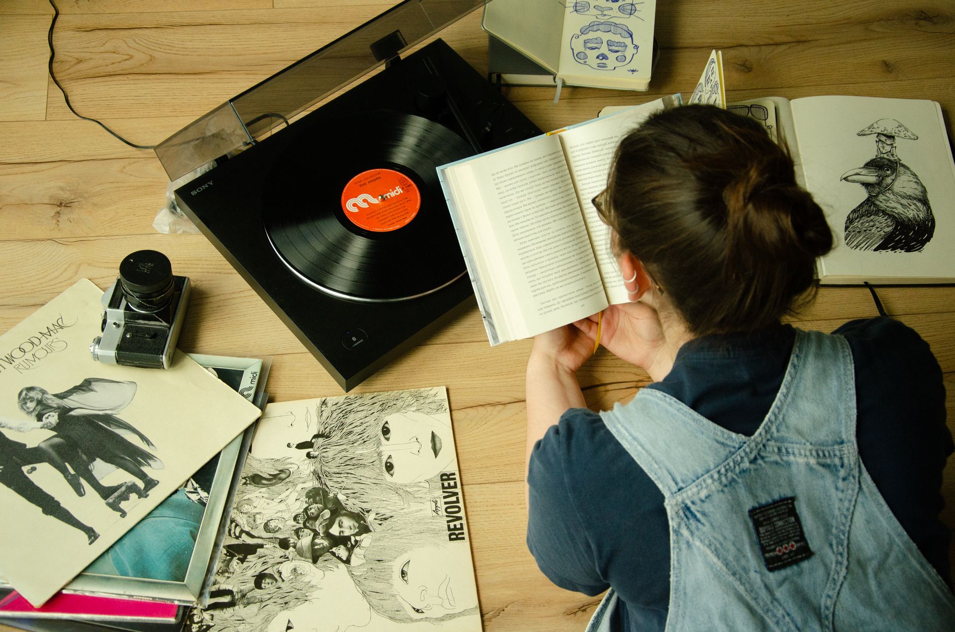 Top view of a woman reading a book surrounded by vinyl records and a turntable.