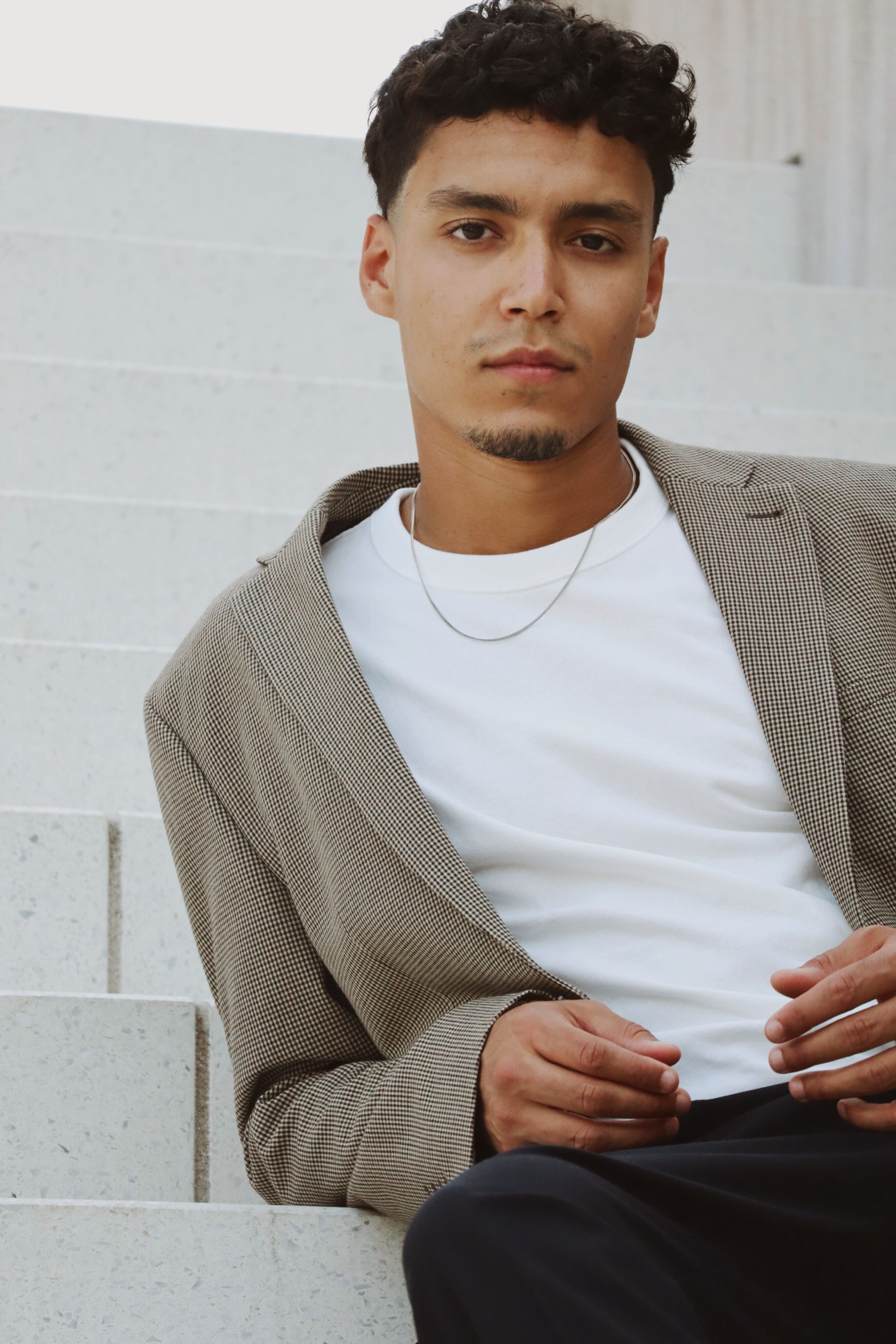 Elegant portrait of a man in a blazer sitting on steps in Berlin, showcasing modern fashion.