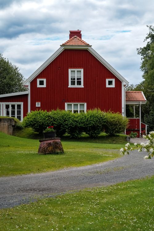 Free A beautiful red wooden house in a serene rural setting with lush greenery and a winding path. Stock Photo