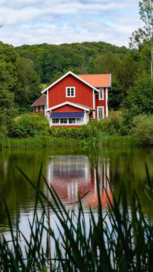Free Beautiful red house with reflection in a tranquil lake surrounded by lush greenery. Stock Photo