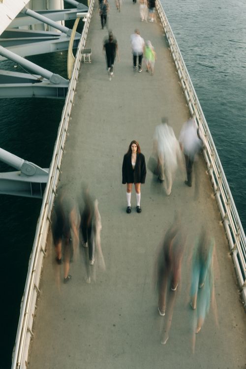 Free A woman stands still on a bustling footbridge, capturing a moment of solitude amidst motion. Stock Photo