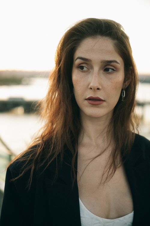 Free Stylish woman with long hair in a black jacket gazing away outdoors at sunset. Stock Photo