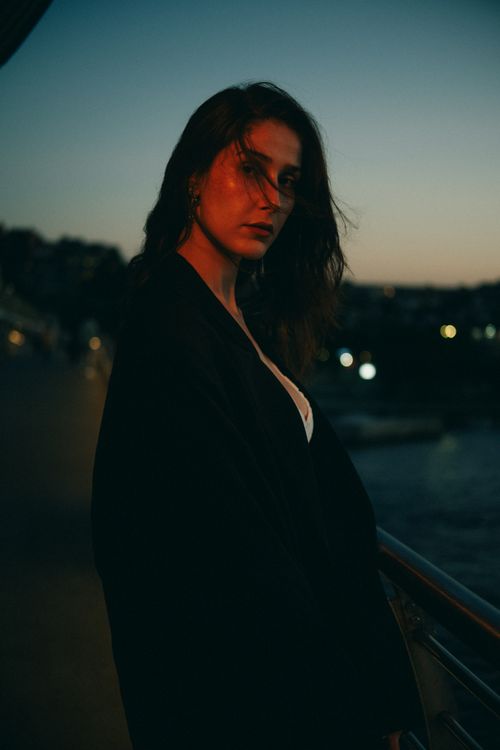 Free Artistic portrait of a woman in a black coat at sunset with an urban backdrop. Stock Photo