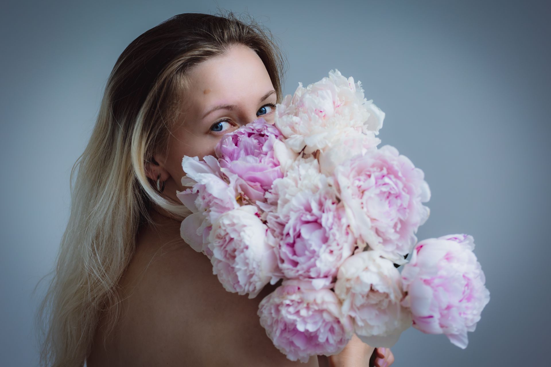 Young woman poses with pink peonies in a studio setting, exuding elegance and beauty.