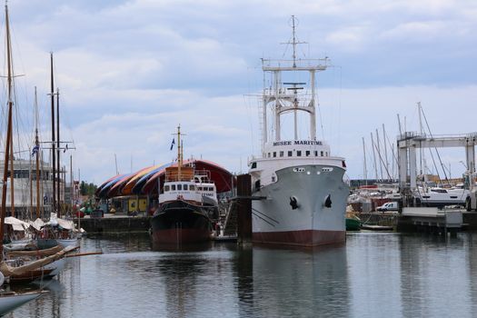 A maritime museum ship docked in a harbor surrounded by colorful structures and watercraft.