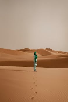 A solitary figure stands in the vast desert dunes of Merzouga, Morocco, creating a serene and contemplative scene.